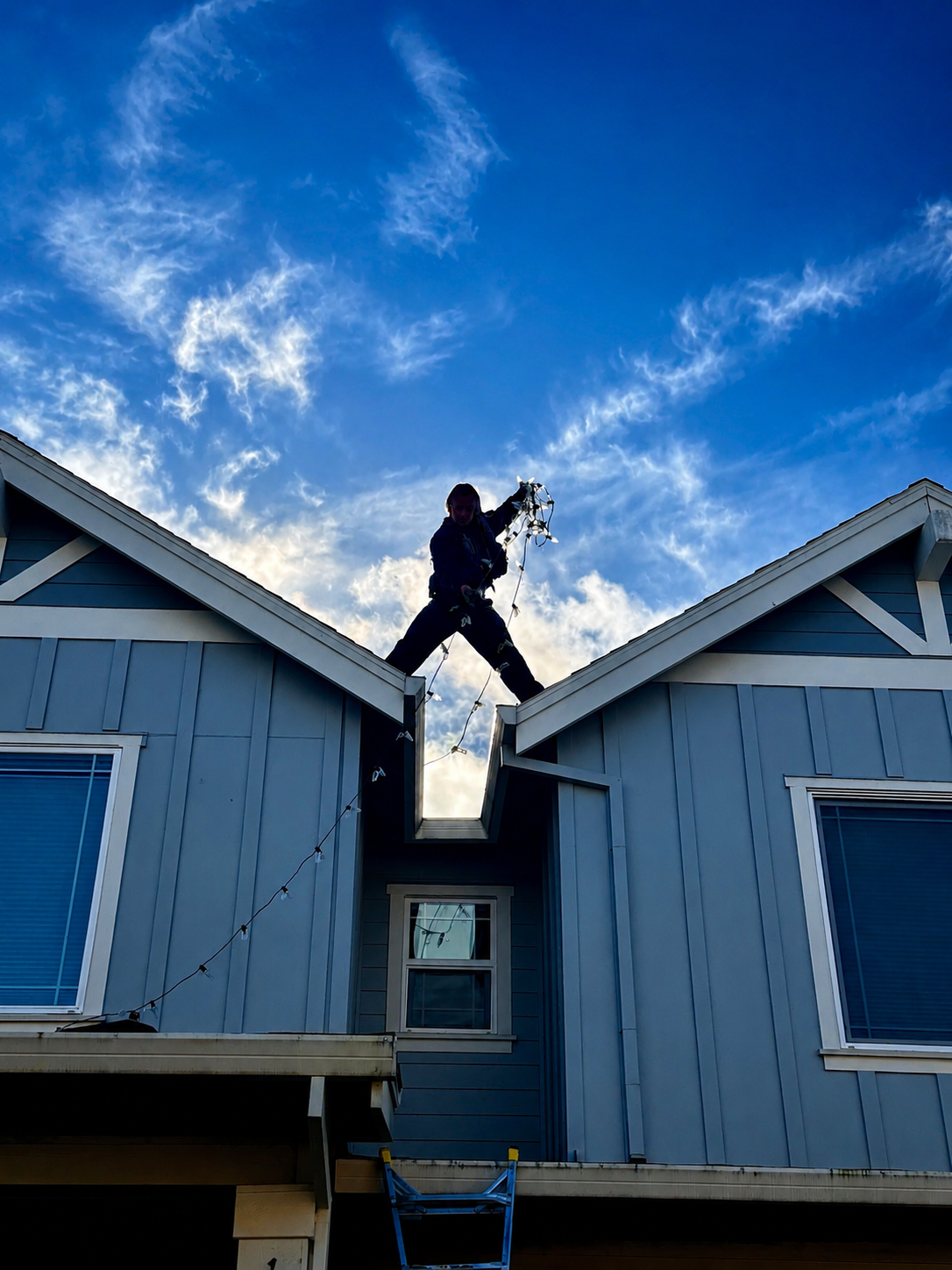 Halen Homes installer silhouetted between rooftop peaks at dusk during a professional Christmas light installation in Oregon