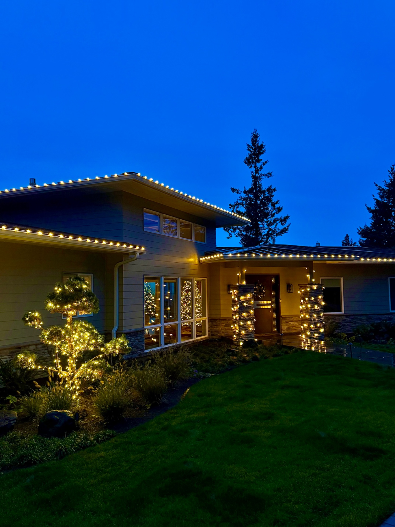 Finished nighttime Christmas lighting project on an Oregon home with warm white lights on roofline and wrapped trees
