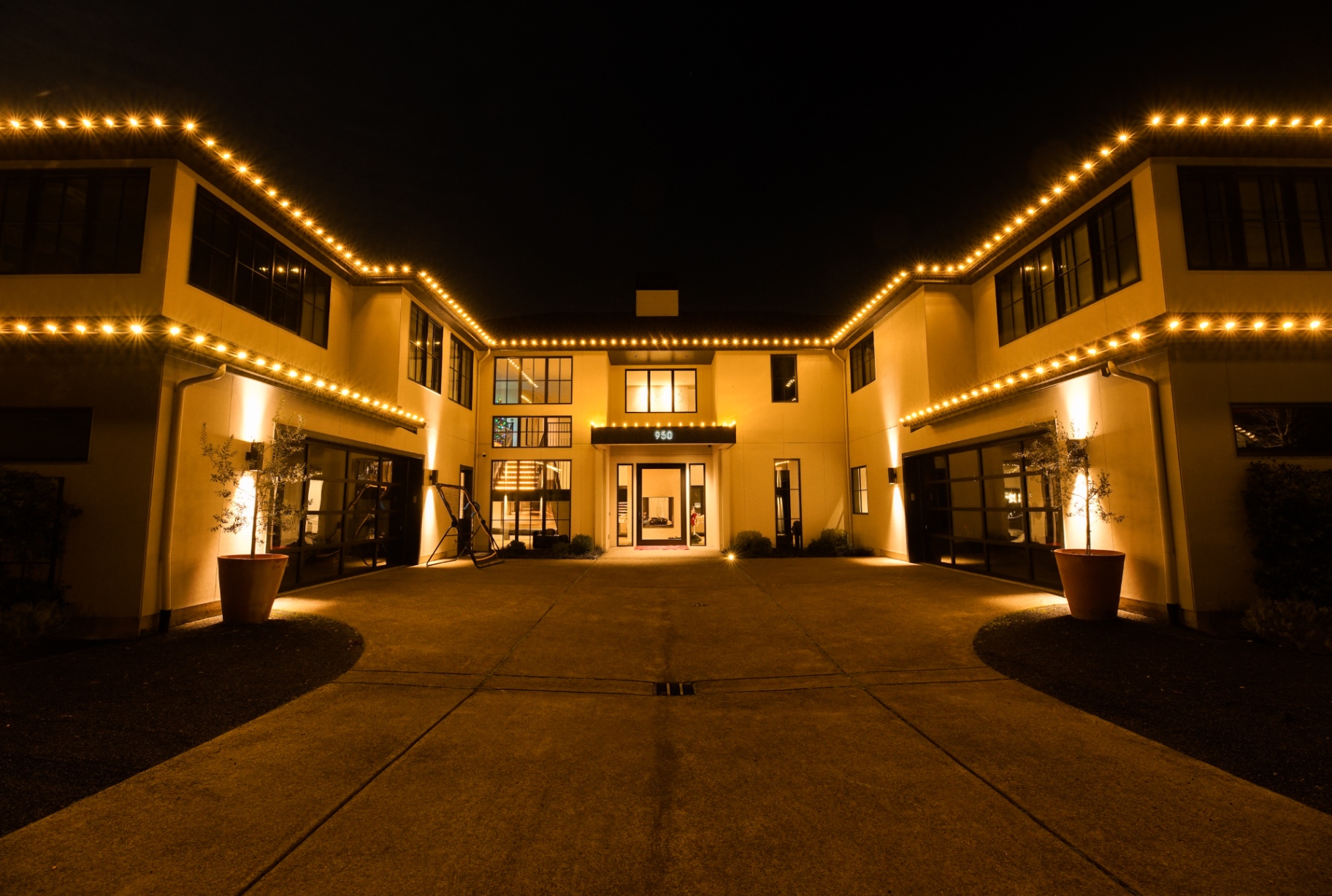 Grand estate courtyard entry outlined in warm-white C9 Christmas lights with uplit olive trees