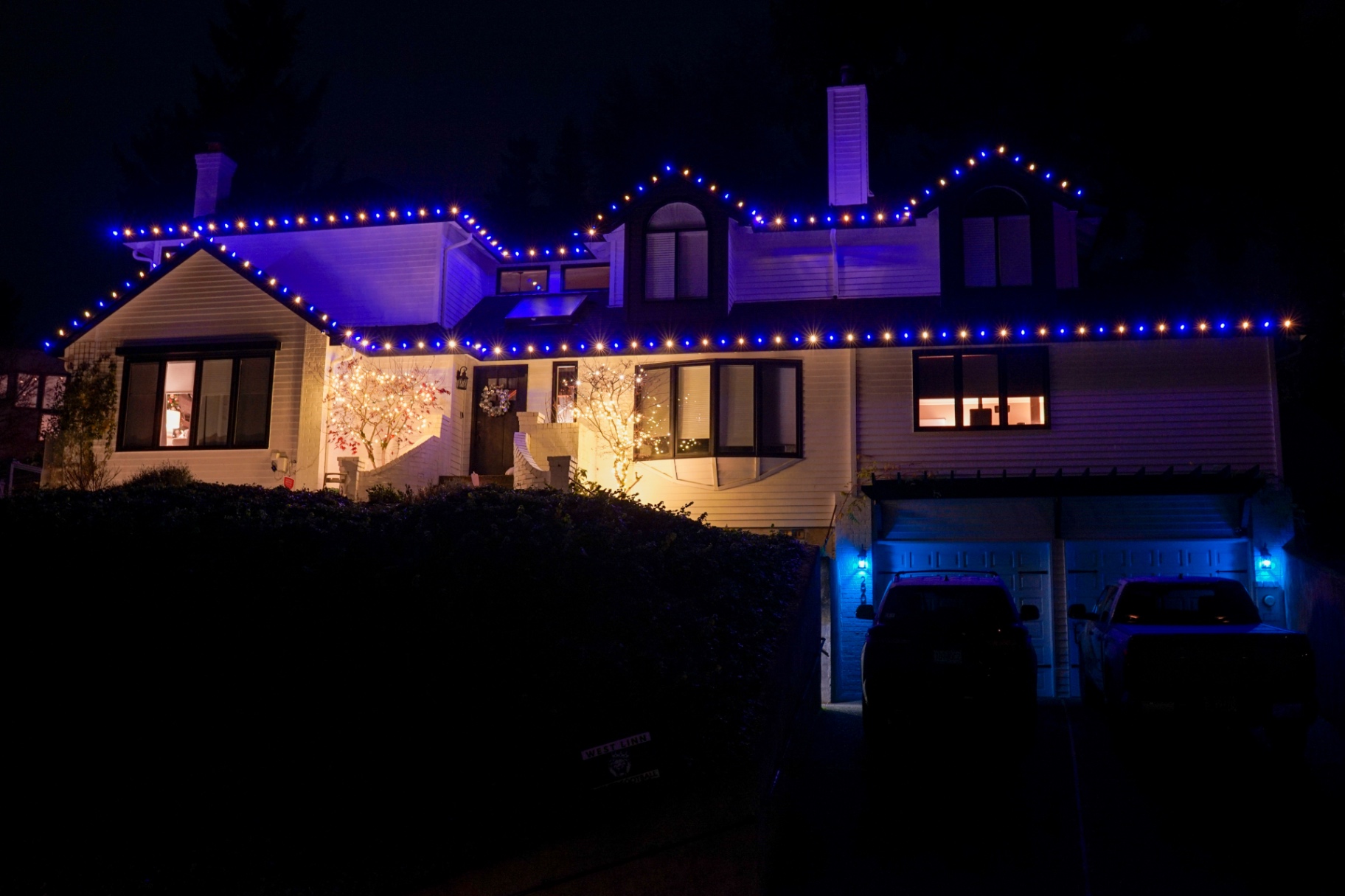 White two-story home with blue and warm-white C9 Christmas lights along the roofline at night