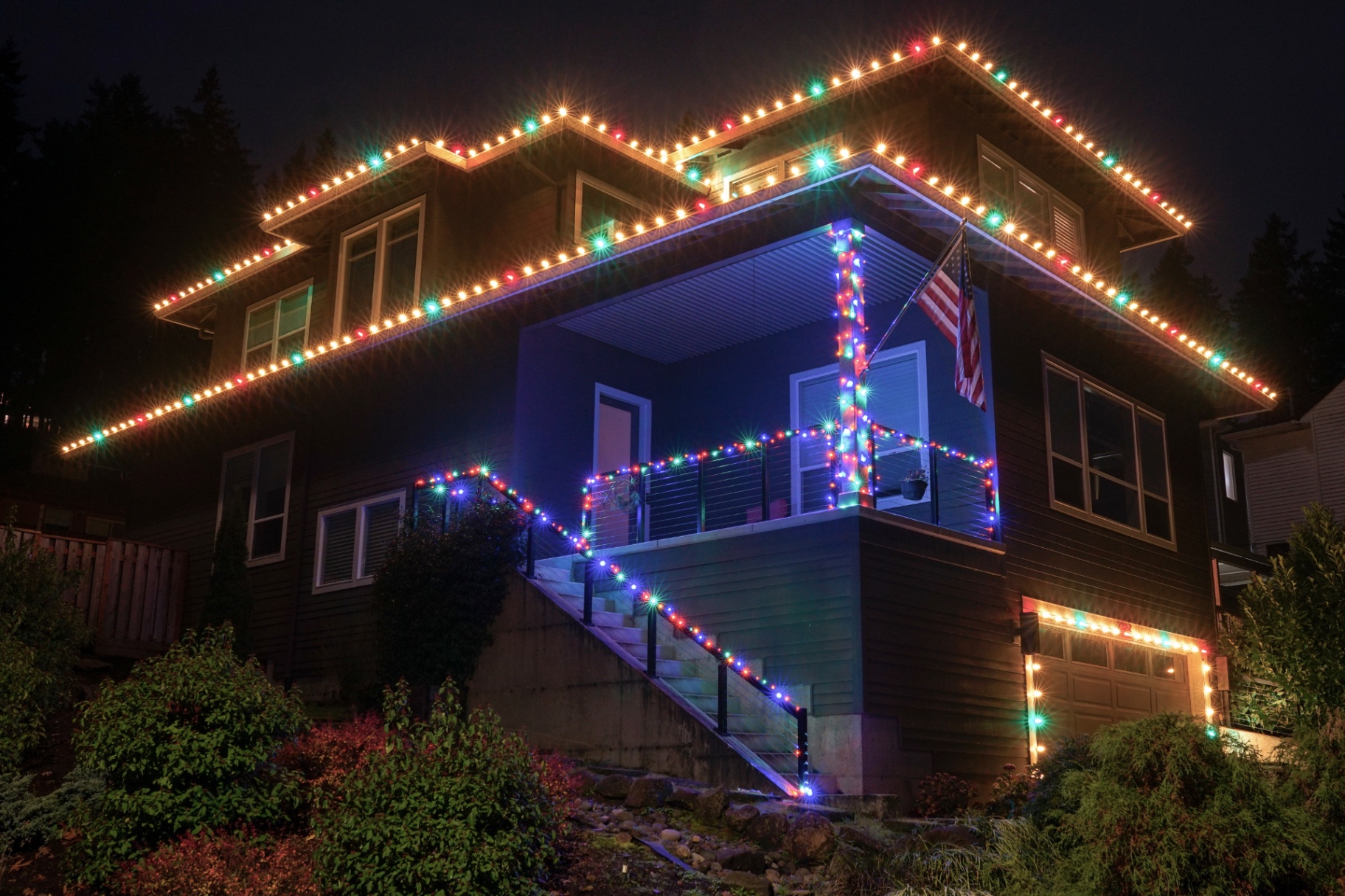 Hillside Oregon home with warm-white roofline lights and multi-color wrapped stairs, railings and columns
