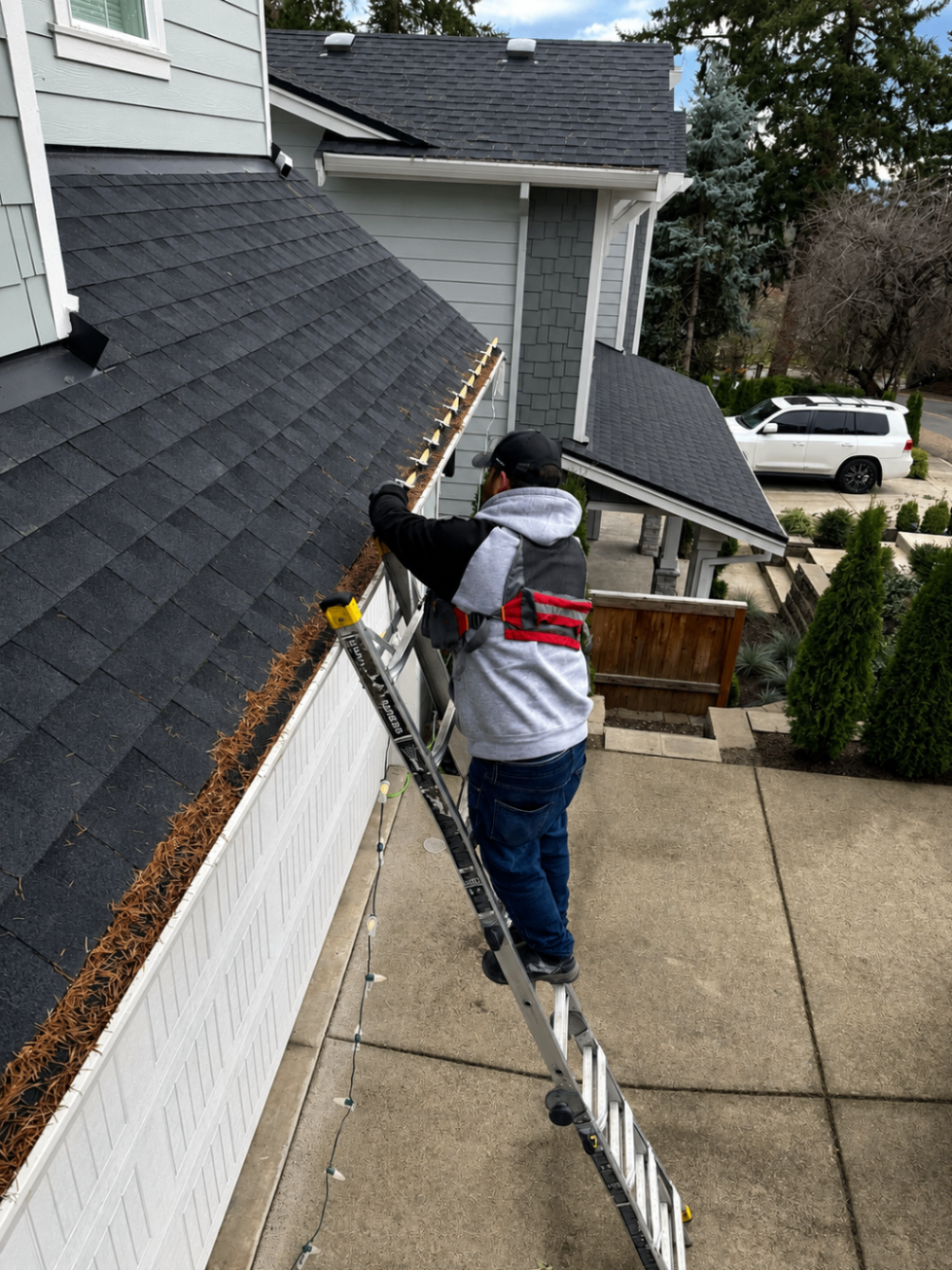 Halen Homes technician on a ladder custom-fitting commercial-grade Christmas lights to a roofline