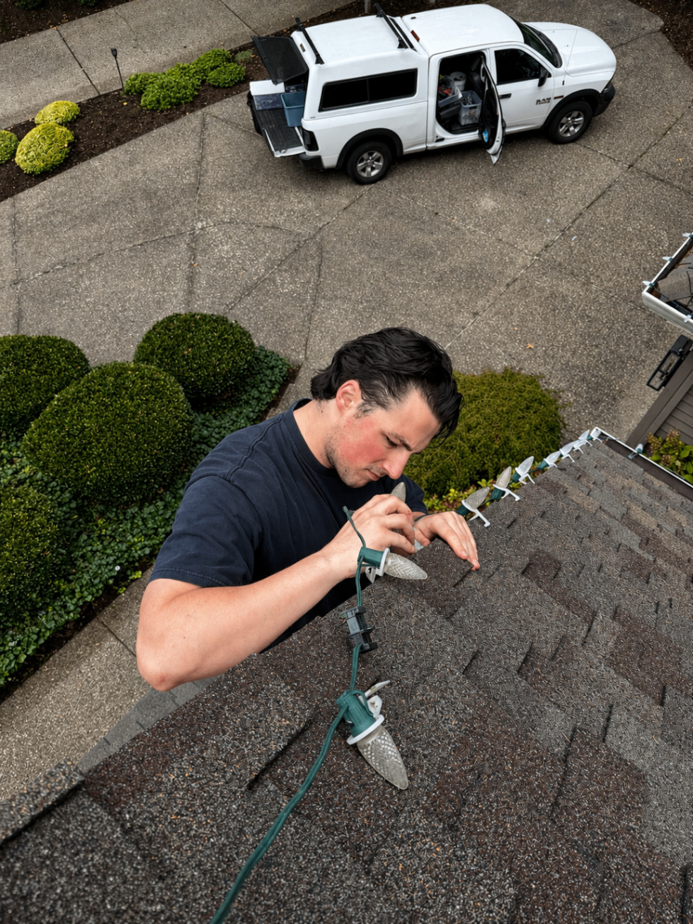 Halen Homes technician on a ladder professionally installing commercial-grade Christmas lights on a home's roofline