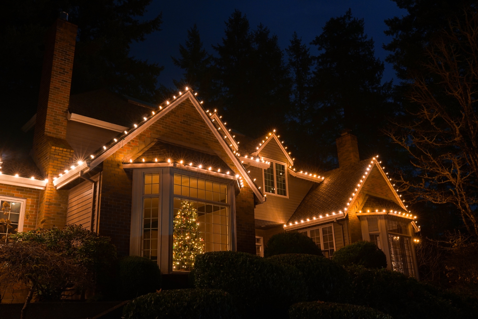 Brick and cedar Oregon home glowing with warm-white C9 Christmas lights along every peak and gable at night